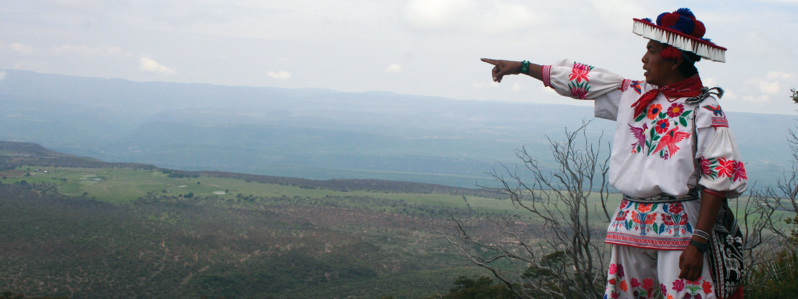 A man in traditional Huichol clothing pointing to the horizon in Mexico