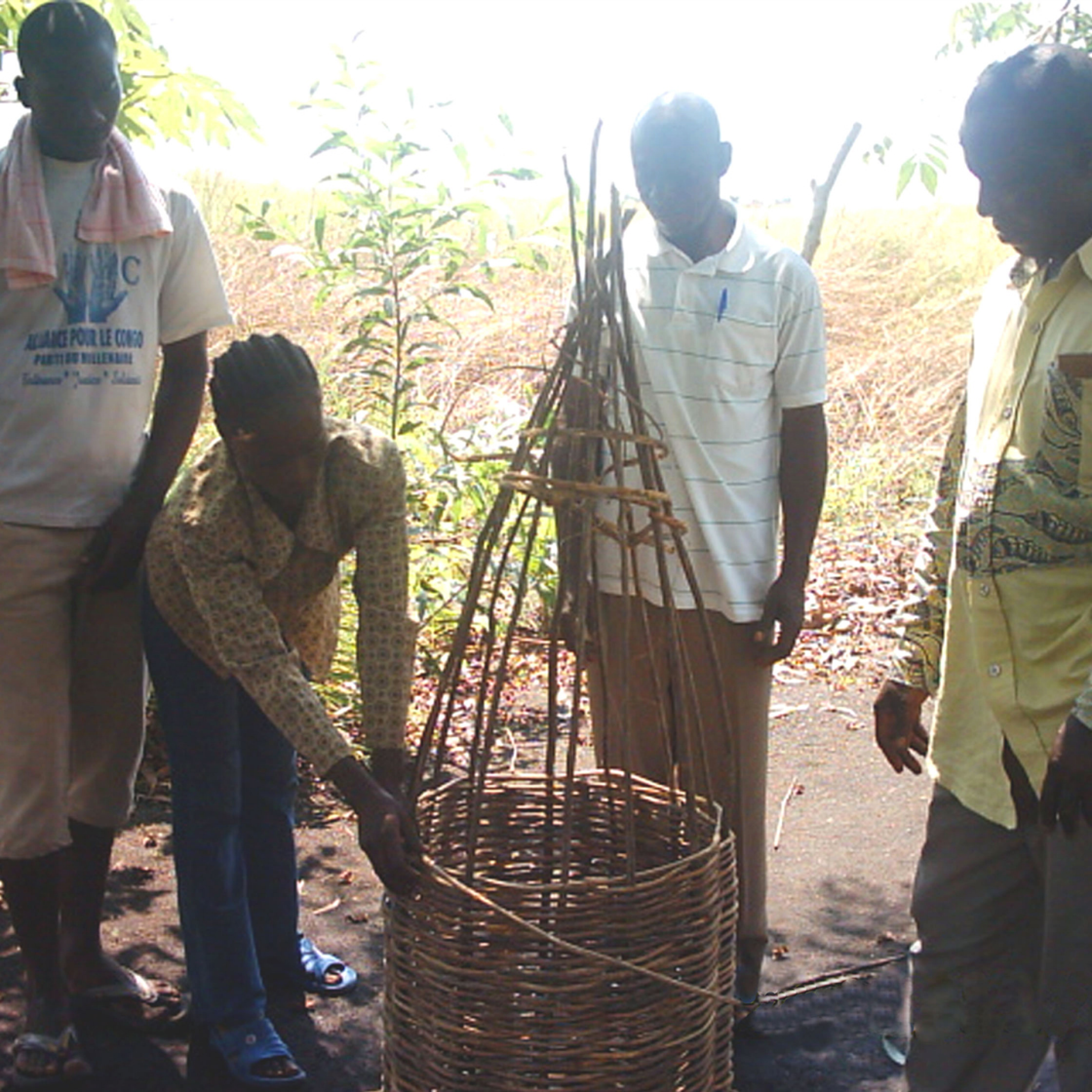 Three men watching a woman weaving a traditional beehive