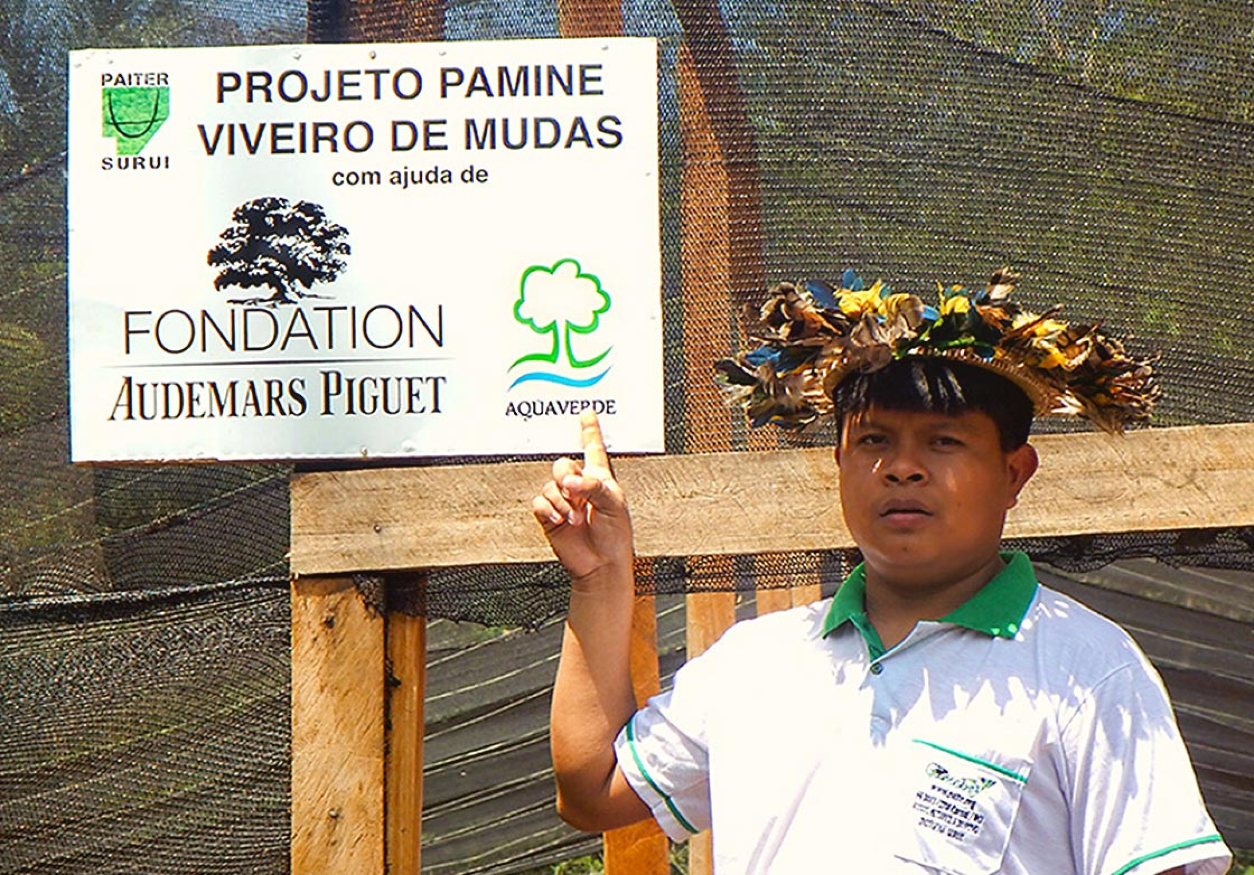 A man posing in front of the sign of the collaboration between Audemars Piguet and the Surui to rebuild their forest heritage